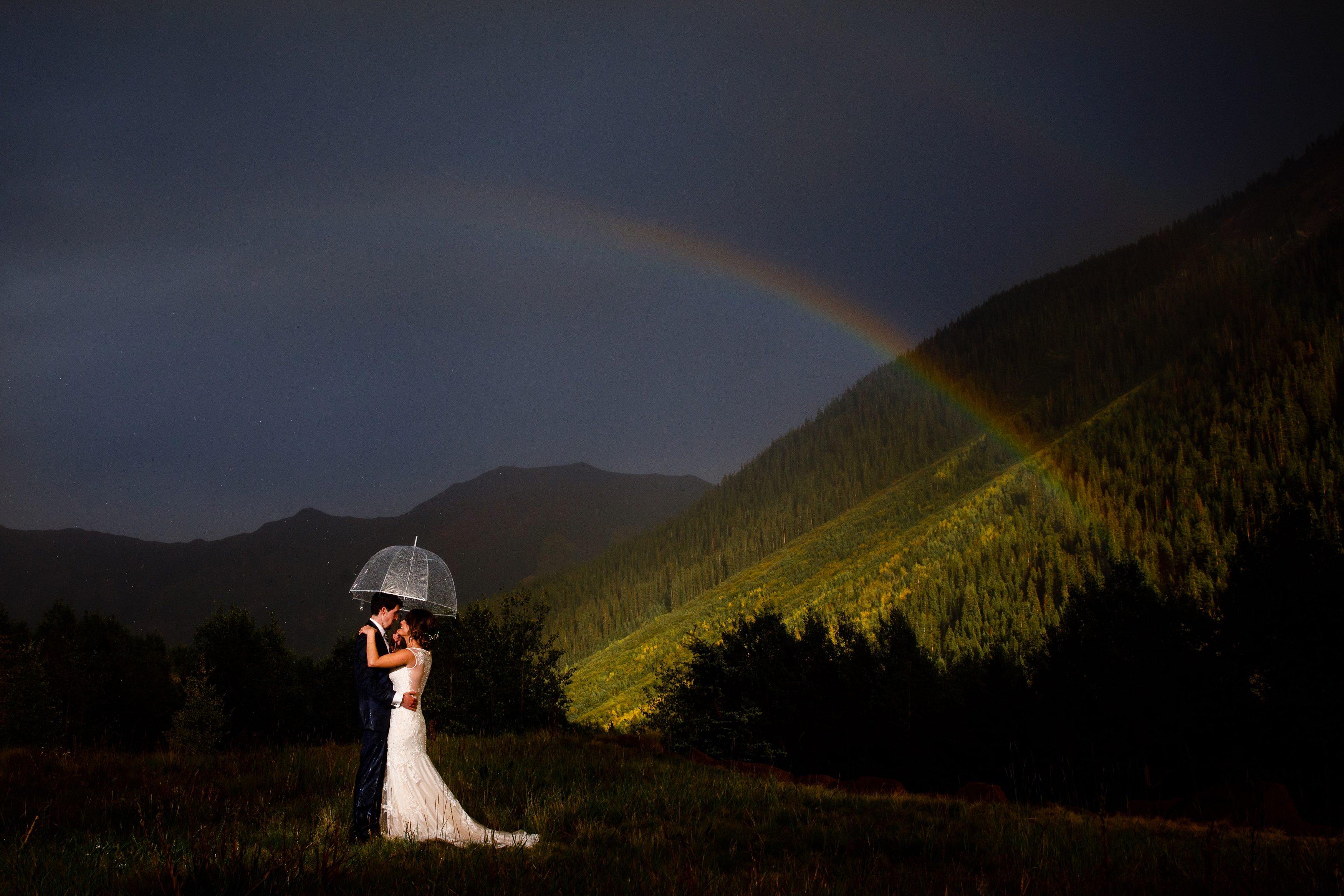 The bride & groom standing below a rainbow after their rainy Maroon Bells Wedding.