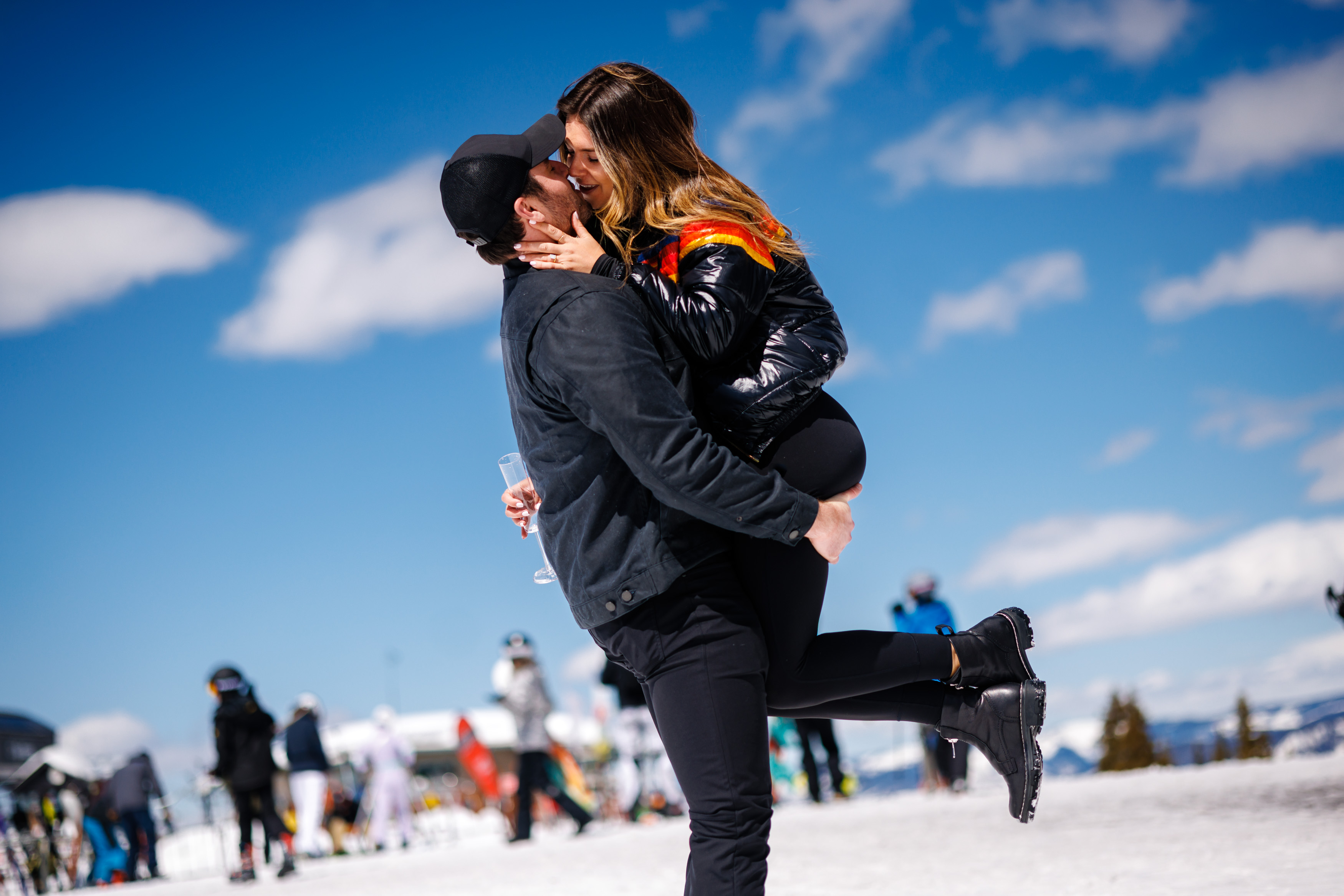 Zach lifts Molley up and the two share a kiss with a glass of champagne just after their Proposal on Aspen Mountain.