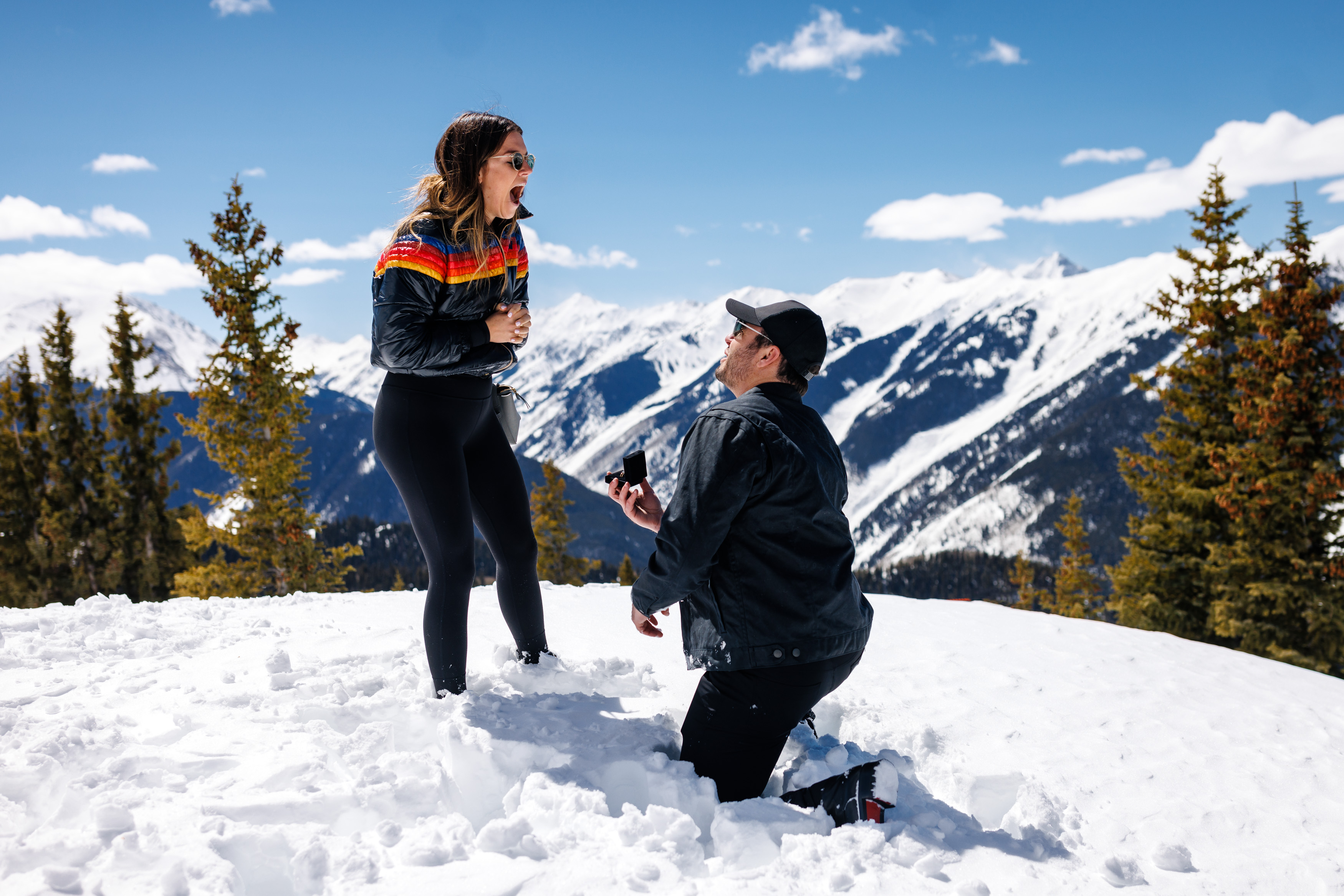 Zach on one knee with wedding ring in hand as he asks Molley to marry him on top of Aspen Mountain.